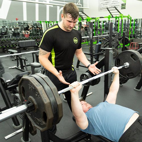 personal trainer helping gym member lift weights